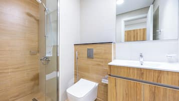 A modern bathroom with a glass-enclosed shower, a wooden vanity, and a white toilet.