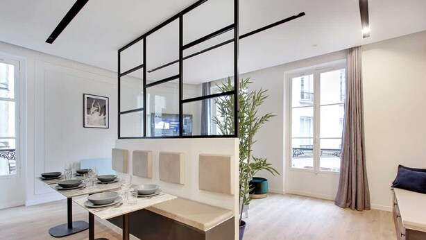 Un salon moderne comprenant un coin repas, un grand miroir, une plante en pot et une vue sur l’extérieur.