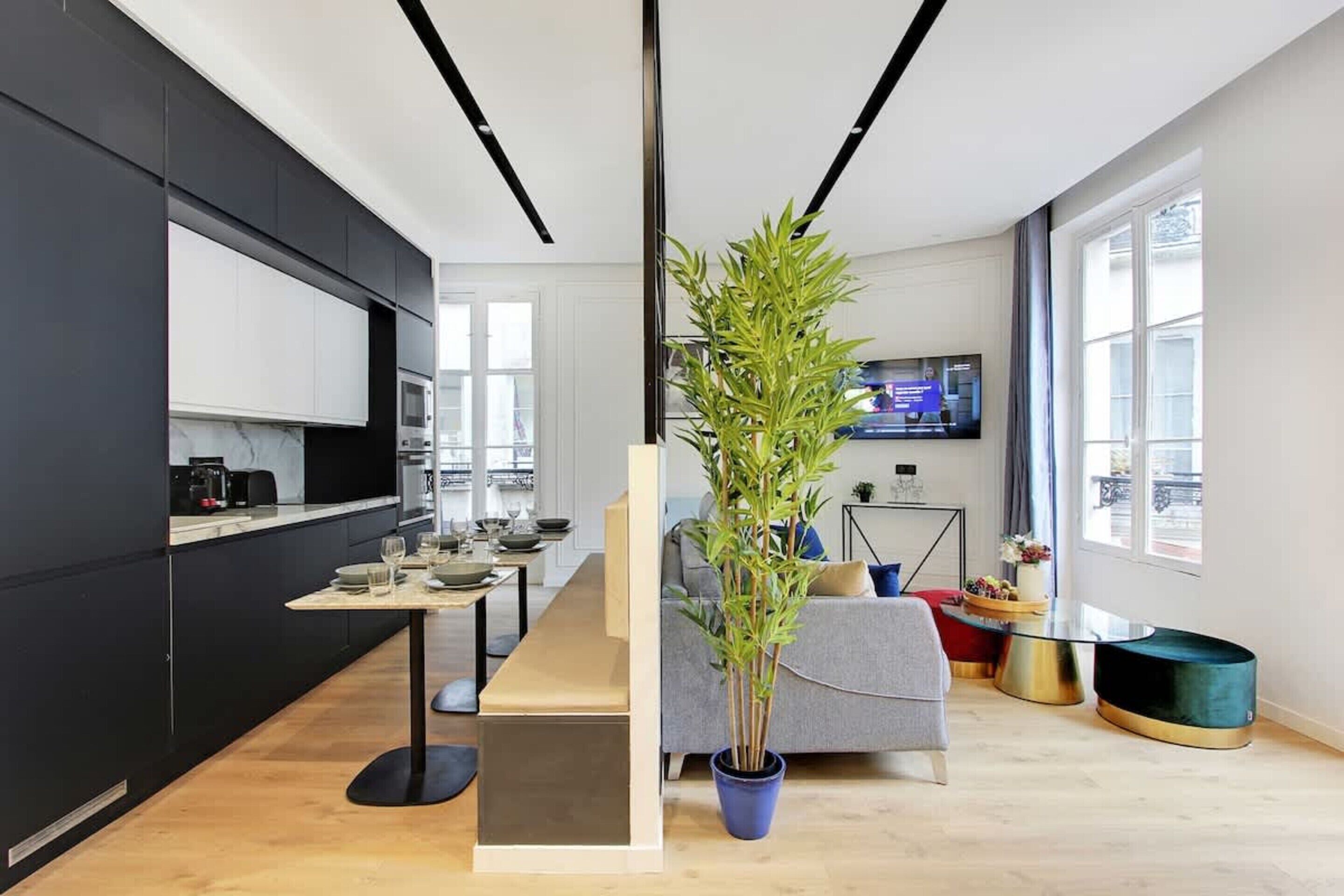 Une cuisine moderne avec des meubles de couleur sombre, un îlot central et un coin repas comprenant un canapé et une table basse.