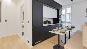 Une cuisine moderne avec des meubles noirs, un plan de travail blanc et un coin repas avec une table dressée pour quatre personnes.