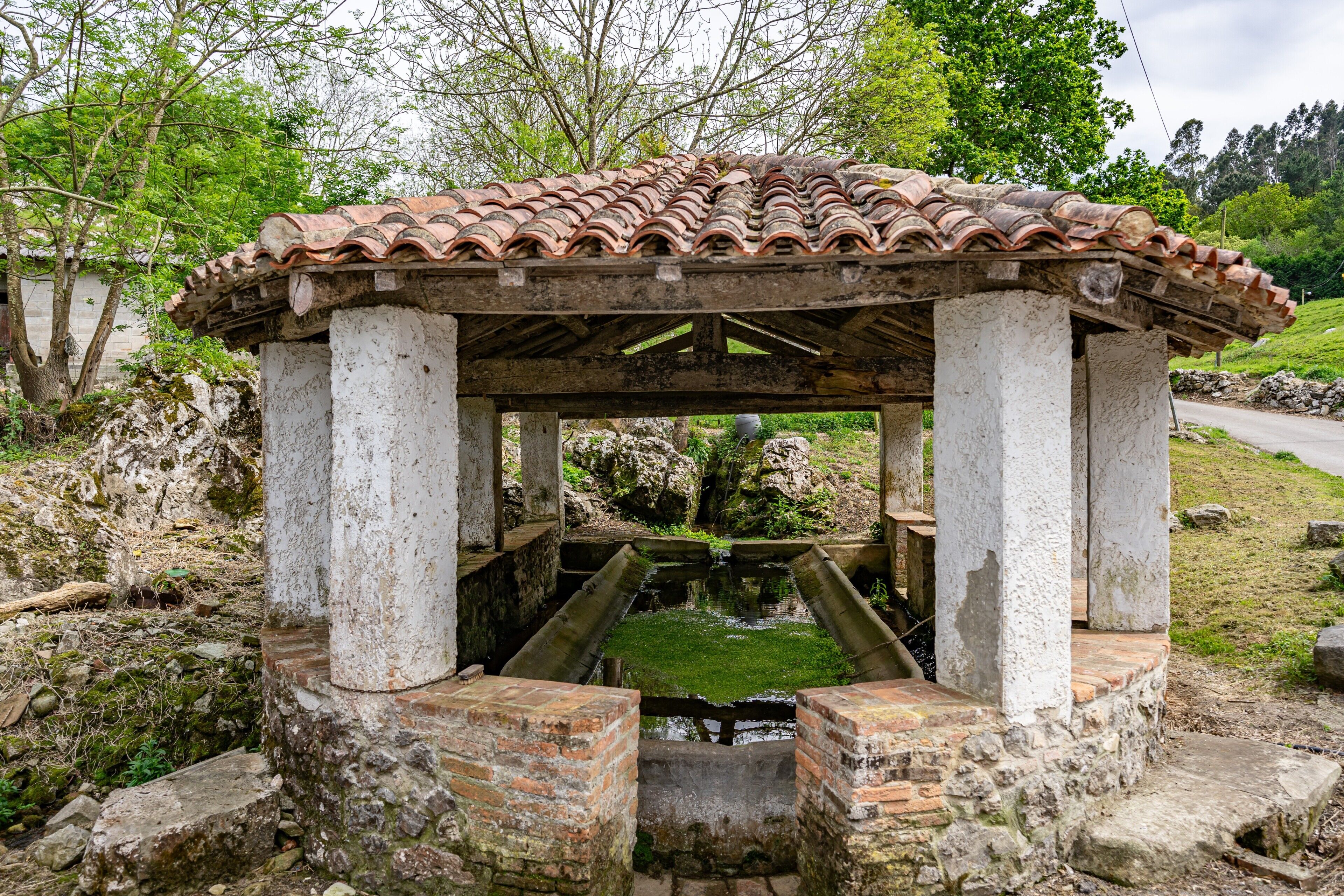 A traditional stone structure with a tiled roof, a central water feature, and a surrounding stone wall.