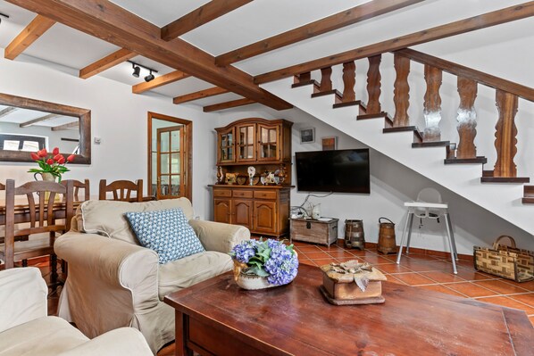A living room with a wooden staircase, a television, and a dining area with chairs and a table.
