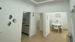 Une cuisine moderne avec des meubles blancs, un coin repas doté d’une table et de chaises blanches, et un couloir menant aux autres pièces.