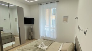 Une chambre moderne avec un grand lit, un miroir, une télévision et une fenêtre ornée de rideaux légers.