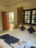 A hotel room with a bed, a window with curtains, a door, and a view of the outside.