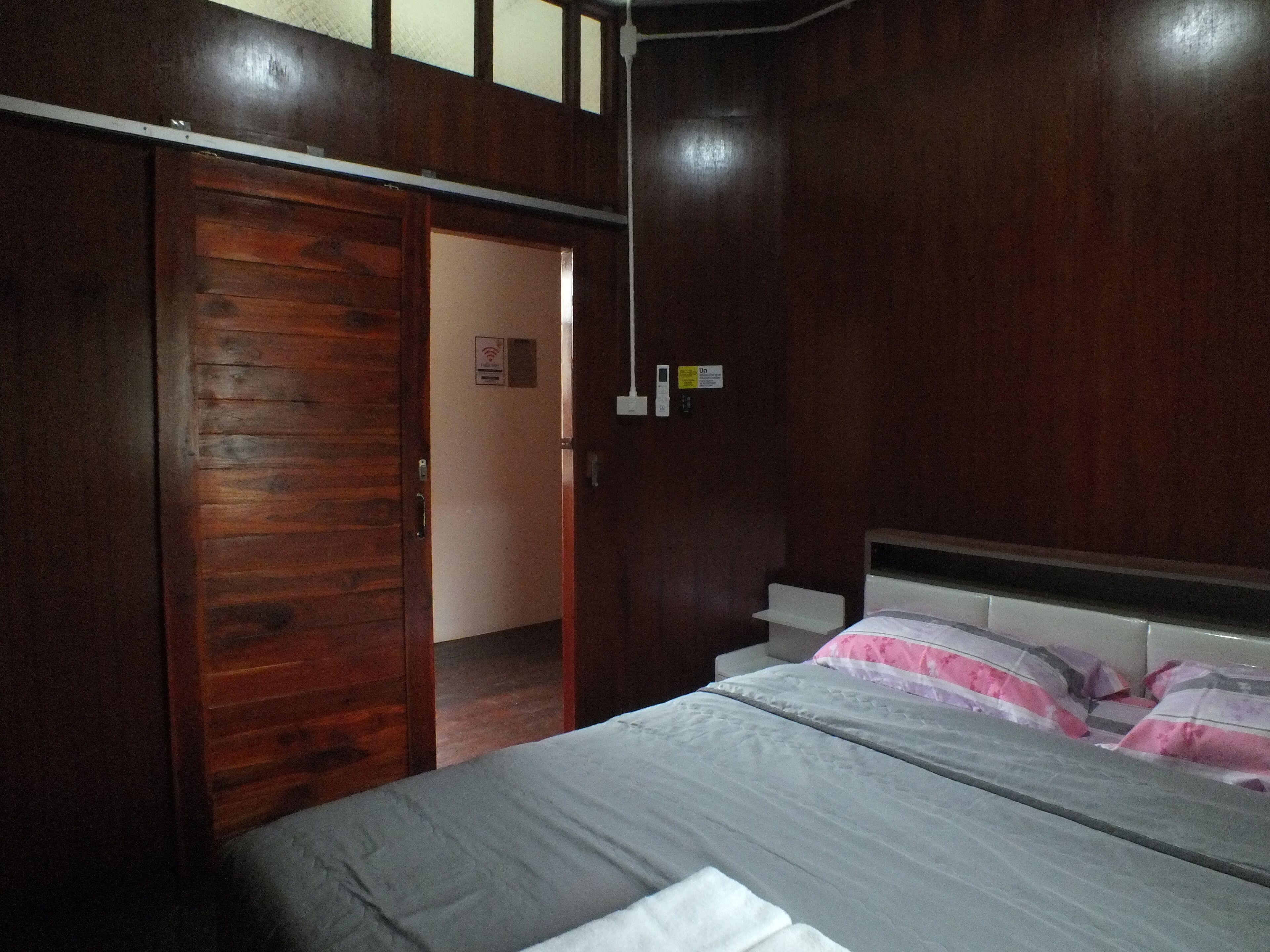 A bedroom with a wooden wardrobe, a bed with a white mattress and pink and white bedding, and a white bedside table.