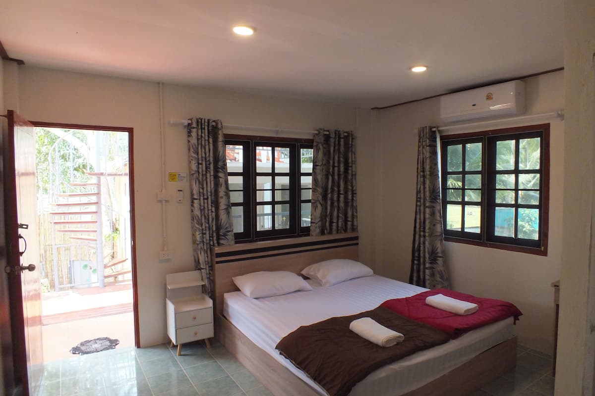 Un dormitorio con una cama, una mesita de noche, una ventana con cortinas y un equipo de aire acondicionado.
