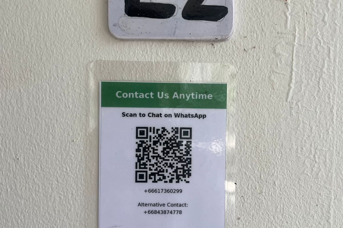 Un letrero con un código QR e información de contacto para un hotel llamado 'Alfartime House' en Somui, que incluye una opción de chat de WhatsApp y dos números de teléfono.