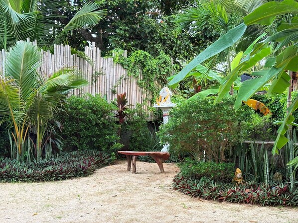 A garden with a wooden fence, a bench, and various tropical plants.