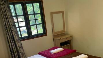 A double bed with white and brown bedding, a wooden nightstand with a mirror, and a window with curtains.