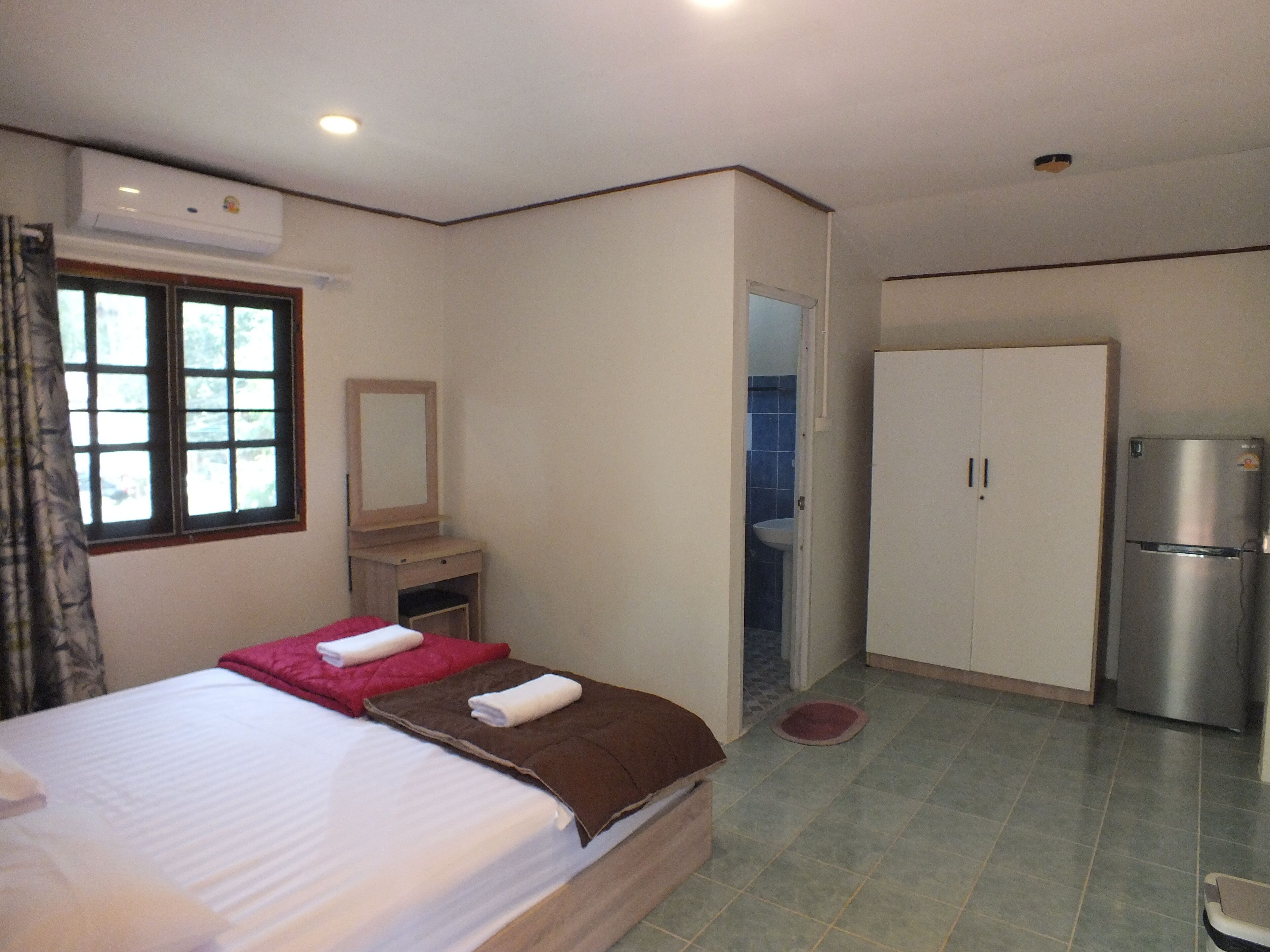 A hotel room with a bed, a wardrobe, a mirror, a sink, and a refrigerator.
