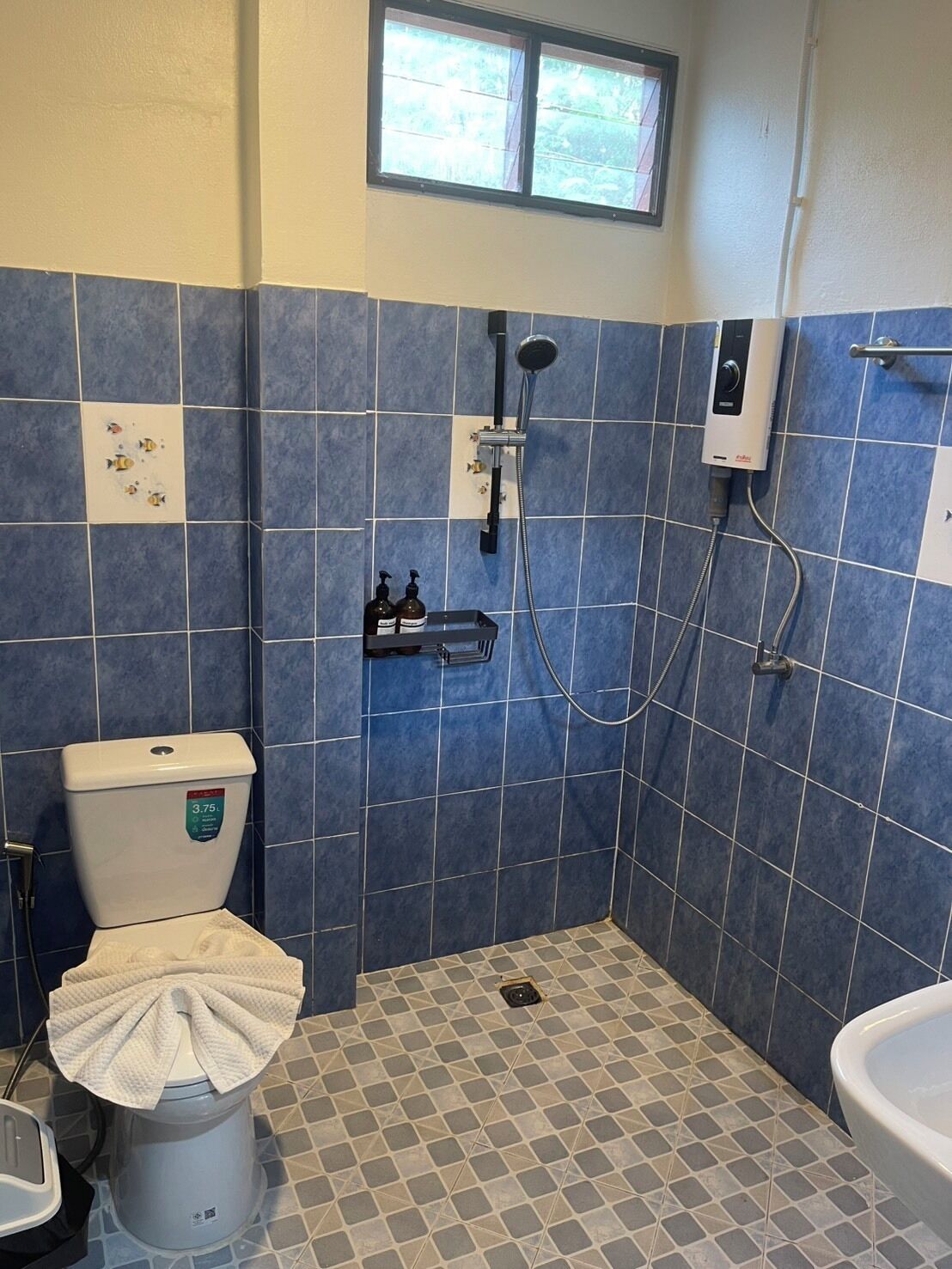 A bathroom with blue tiles, a toilet, a shower, and a window.