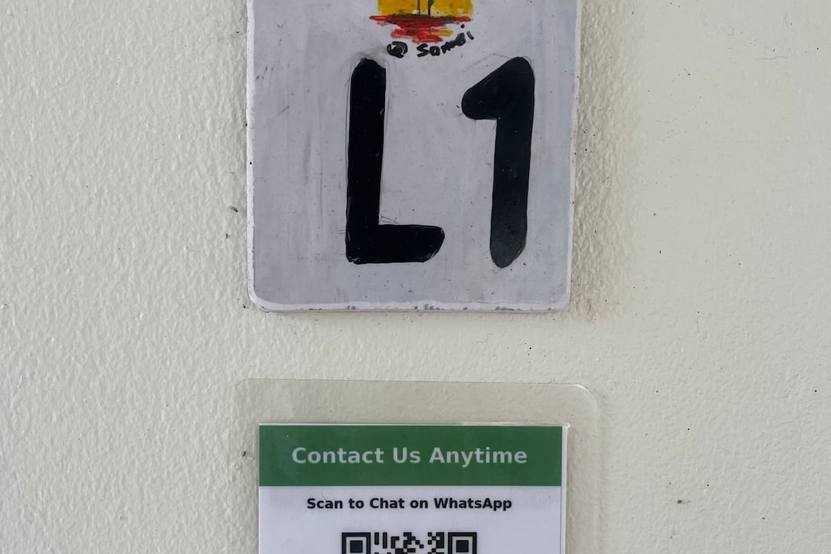 Un letrero fijado a la pared con un código QR, dos números de teléfono y una opción de contacto por WhatsApp.