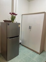 A kitchen with a stainless steel refrigerator, a wooden cabinet, and a tiled floor.