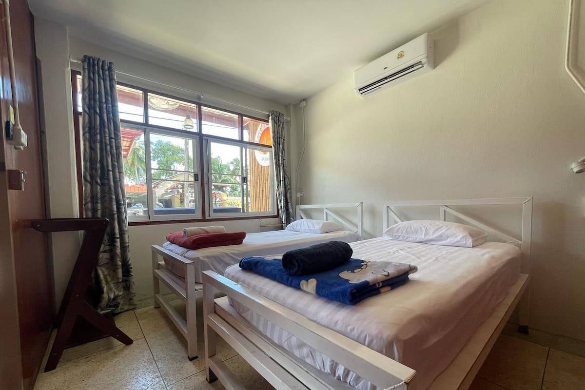 Un dormitorio con dos camas, una ventana con cortinas, un equipo de aire acondicionado y vistas al exterior.