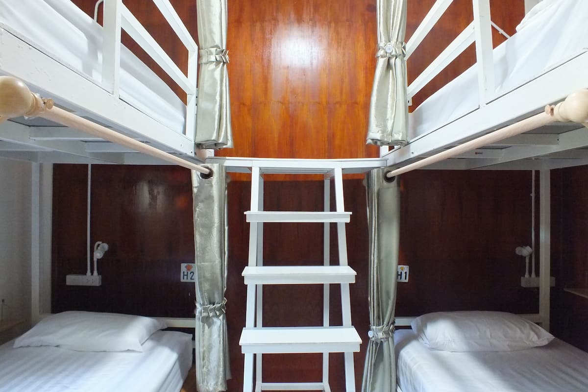 Habitación con literas, una escalera, paredes de madera y camas blancas.