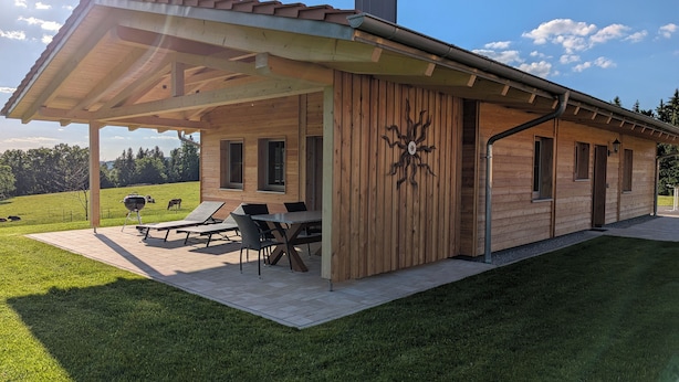 A wooden cabin with a covered patio, outdoor seating, and a chimney. - Vacation chalet with sauna and large terrace at Ferienhof Schiegl in the bay. Forest (Brennberg)