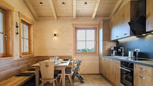 A wooden interior with a dining table, chairs, a kitchen with modern appliances, and a large window. - Vacation chalet with sauna and large terrace at Ferienhof Schiegl in the bay. Forest (Brennberg)