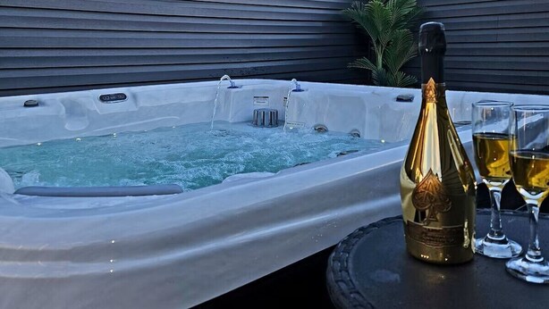 Ein Whirlpool mit fließendem Wasser, eine Champagnerflasche und zwei Gläser auf einem Tisch.