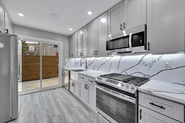 A modern kitchen with white cabinets, a built-in microwave, a gas stove, and a large window overlooking a wooden deck.