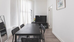 En moderne stue med et mørkt træspisebord, sorte stole, et fladskærms-tv og et stort vindue med lette gardiner.