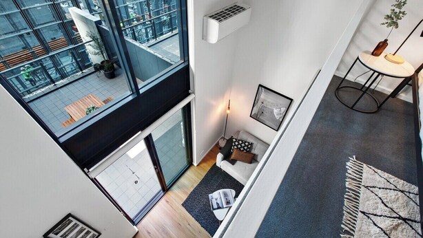 Un interior moderno con techo alto, ventanas grandes, un sofá, una mesita y una planta decorativa.