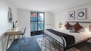 Un dormitorio moderno con cama, escritorio, silla y ventana grande.