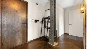 A hallway with a wooden door, a metal rack, and a white wall with a light switch. - Picasso in London (london)