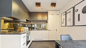 A modern kitchen with stainless steel appliances, a herringbone wood floor, and a dining area with a table and chairs. - Picasso in London (london)