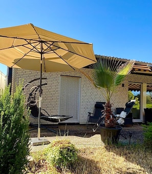 Een patio met een grote parasol, een hangmat, een potpalmpje en zitplaatsen.