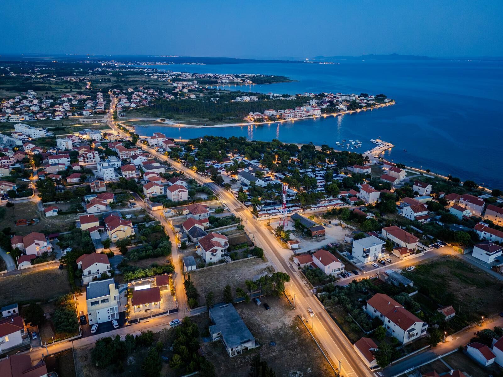 Vista aérea de un pueblo costero al atardecer, con edificios residenciales, un puente y un puerto deportivo.