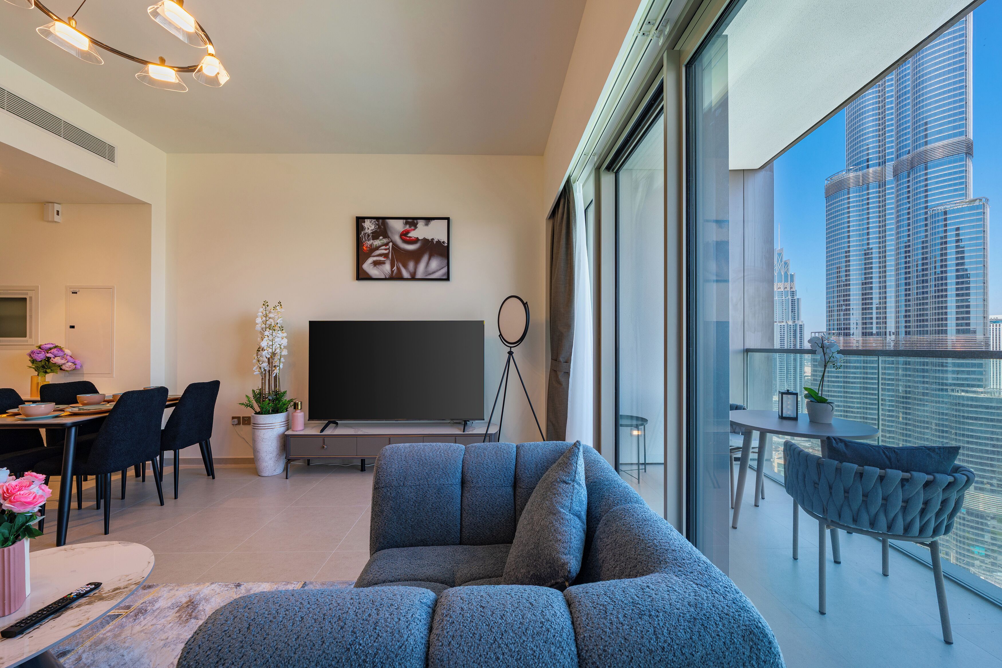 Una sala de estar moderna con un televisor de pantalla plana grande, un sofá, un comedor y un balcón con vista a la ciudad.