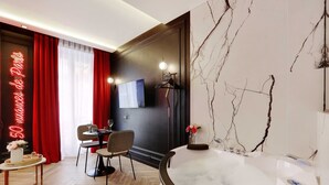 Een moderne hotelkamer met een marmeren badkuip, een zithoek met een tafel en stoelen, en een grote spiegel aan de muur.