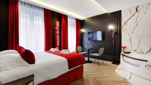 Een hotelkamer met een groot bed, rode gordijnen, een televisie, een kleine tafel met stoelen en een marmeren muur.