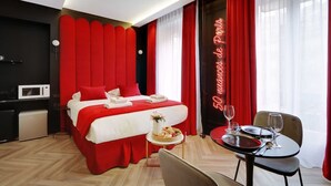 Een hotelkamer met een bed, een eettafel met stoelen, een magnetron en een neonbord.