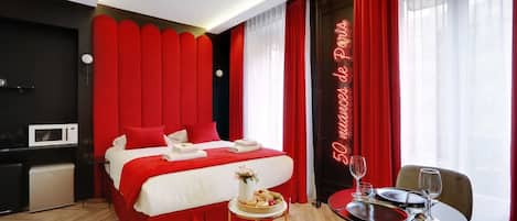 A hotel room with a bed, a dining table with chairs, a microwave, and a neon sign.