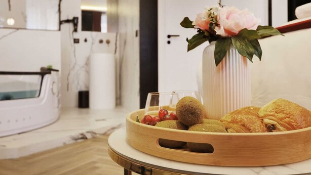 Een moderne badkamer met een witte badkuip, een houten dienblad met gebak en fruit, en een vaas met bloemen.