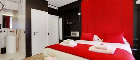A modern hotel room with a large bed, red accent walls, a white door, and a wooden floor.