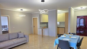 Una sala moderna con un sofá, una mesa de comedor preparada para cuatro personas y una cocina al fondo.