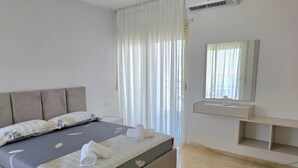 Un dormitorio con cama, mesita de noche, espejo y ventana con cortinas.