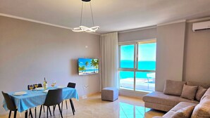 A dining area with a table set for four, a sofa, and a TV displaying a beach scene.