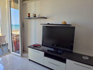 Een moderne woonkamer met een flatscreen televisie, een glazen deur naar een balkon en een minimalistische inrichting.