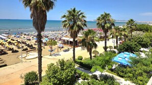 A beach with palm trees, umbrellas, and beach chairs. - Beachfront & Sea View Apartment 102 (Durres)