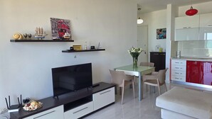 A modern living room with a flat-screen TV, a dining table with chairs, and a kitchen area with white cabinets and red appliances. - Beachfront & Sea View Apartment 102 (Durres)