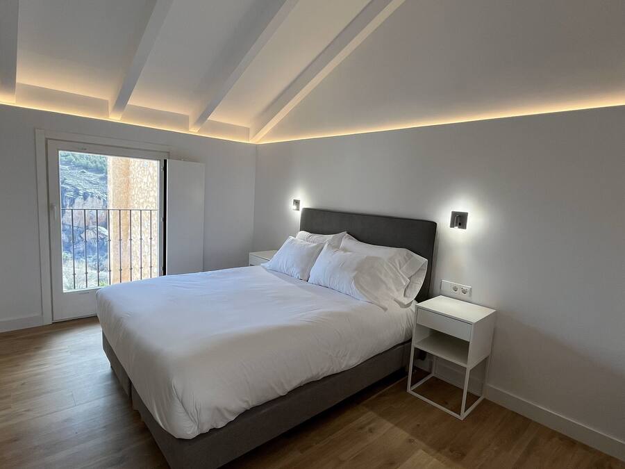 Un dormitorio moderno con una cama grande, una mesita de noche y una ventana con vistas a un paisaje rocoso.