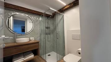 A modern bathroom with a glass shower enclosure, a round mirror, and a wooden vanity.