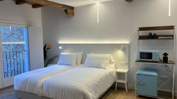 Une chambre comprenant un lit, des tables de chevet, une commode, une lampe fixée au mur, une fenêtre avec vue et une kitchenette équipée d’un four à micro-ondes et d’un petit réfrigérateur.