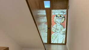 A hallway with a wooden staircase, a tiled floor, and a door with a colorful illustration. - Mirador Del Rey (Cuenca)
