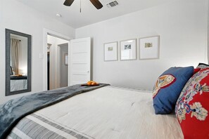 A bedroom with a bed, a ceiling fan, a door, and framed pictures on the wall.