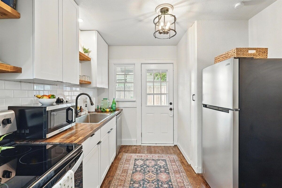 A kitchen with white cabinets, a black microwave, a stainless steel refrigerator, and a patterned rug.